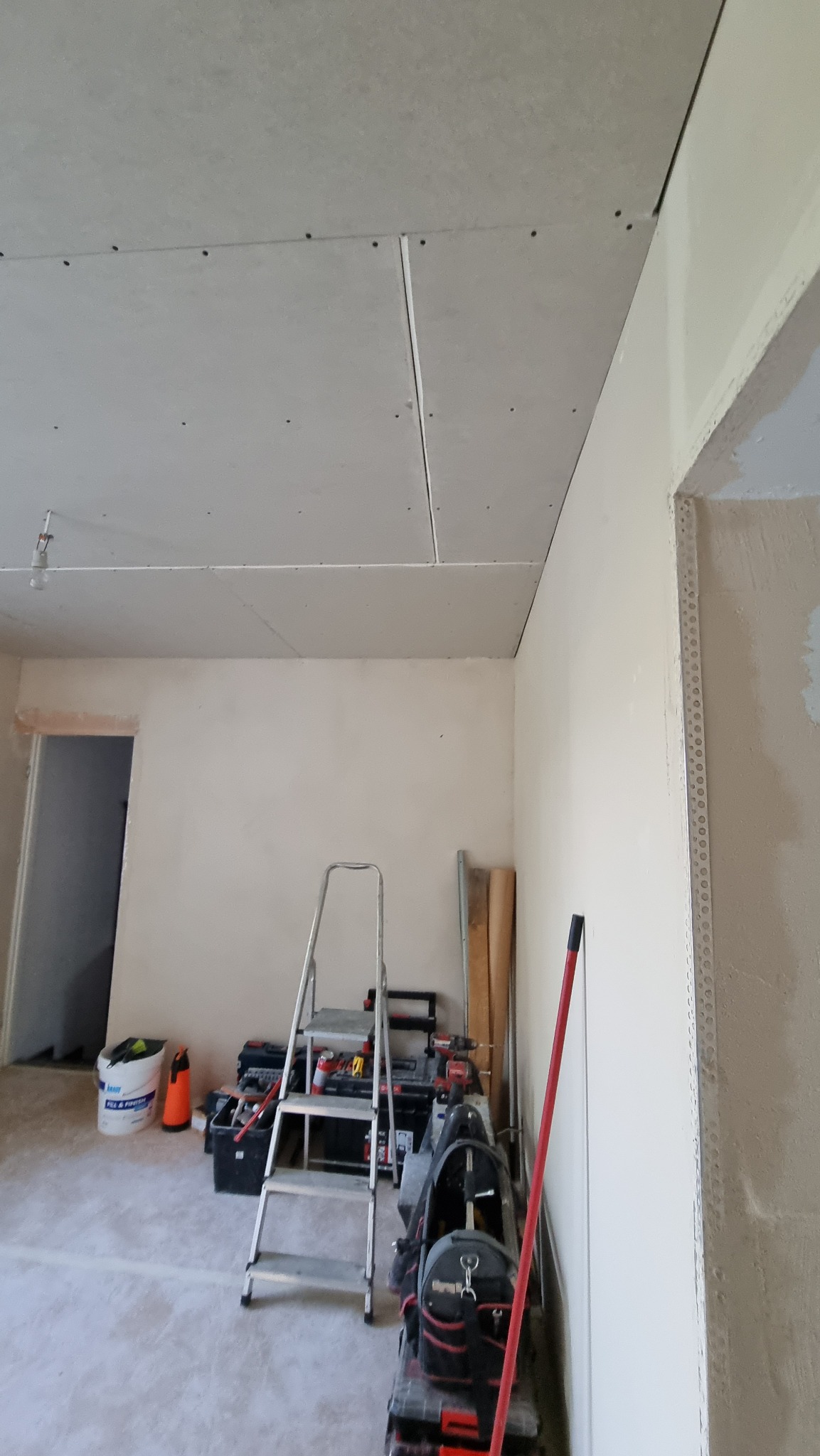 Wnętrze w trakcie remontu: zamontowane płyty karton-gips na suficie, widoczne narzędzia, drabina i profile przy ścianie. Świeża instalacja, przygotowanie do dalszych prac wykończeniowych.