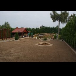 Visual Garden - Widok ogólny ogrodu po założeniu trawnika, z widocznym kręgiem z kamieni, domkiem ogrodowym i wysokimi tujami w tle.