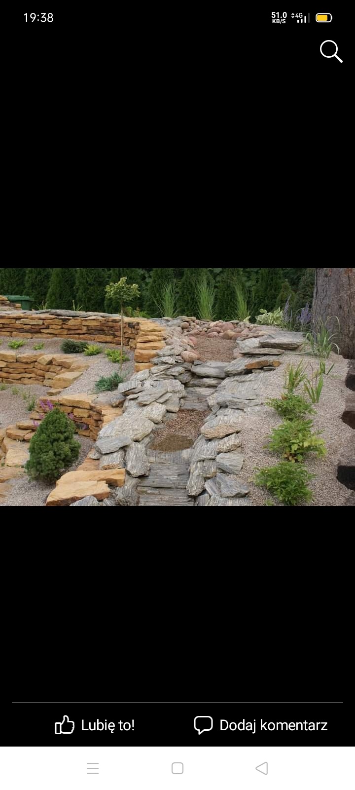 Kaskadowy ogród skalny z elementami wodnymi i roślinnością, wykonany z różnych rodzajów kamienia i żwiru.