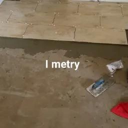 Układanie podłogi z drewnopodobnych płytek, widoczne krzyżyki dystansowe, szpachelka, nóż do tapet i zaprawa klejowa.