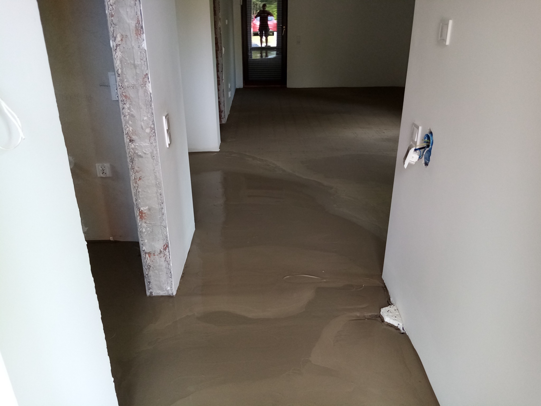 Wylewka podłogowa samopoziomująca w trakcie schnięcia w nowym mieszkaniu, widoczne przygotowane ściany pod malowanie i wystające kable elektryczne.