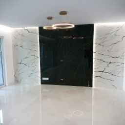 Nowoczesne wnętrze z błyszczącą podłogą, ścianami wykończonymi panelami imitującymi marmur w kolorze białym i czarnym, oraz designerskimi, okrągłymi lampami wiszącymi.