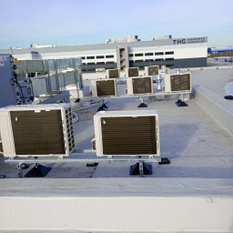 IDP Sp. z o.o. - Rząd klimatyzatorów zamontowanych na dachu budynku przemysłowego z widocznym logo THG w tle.