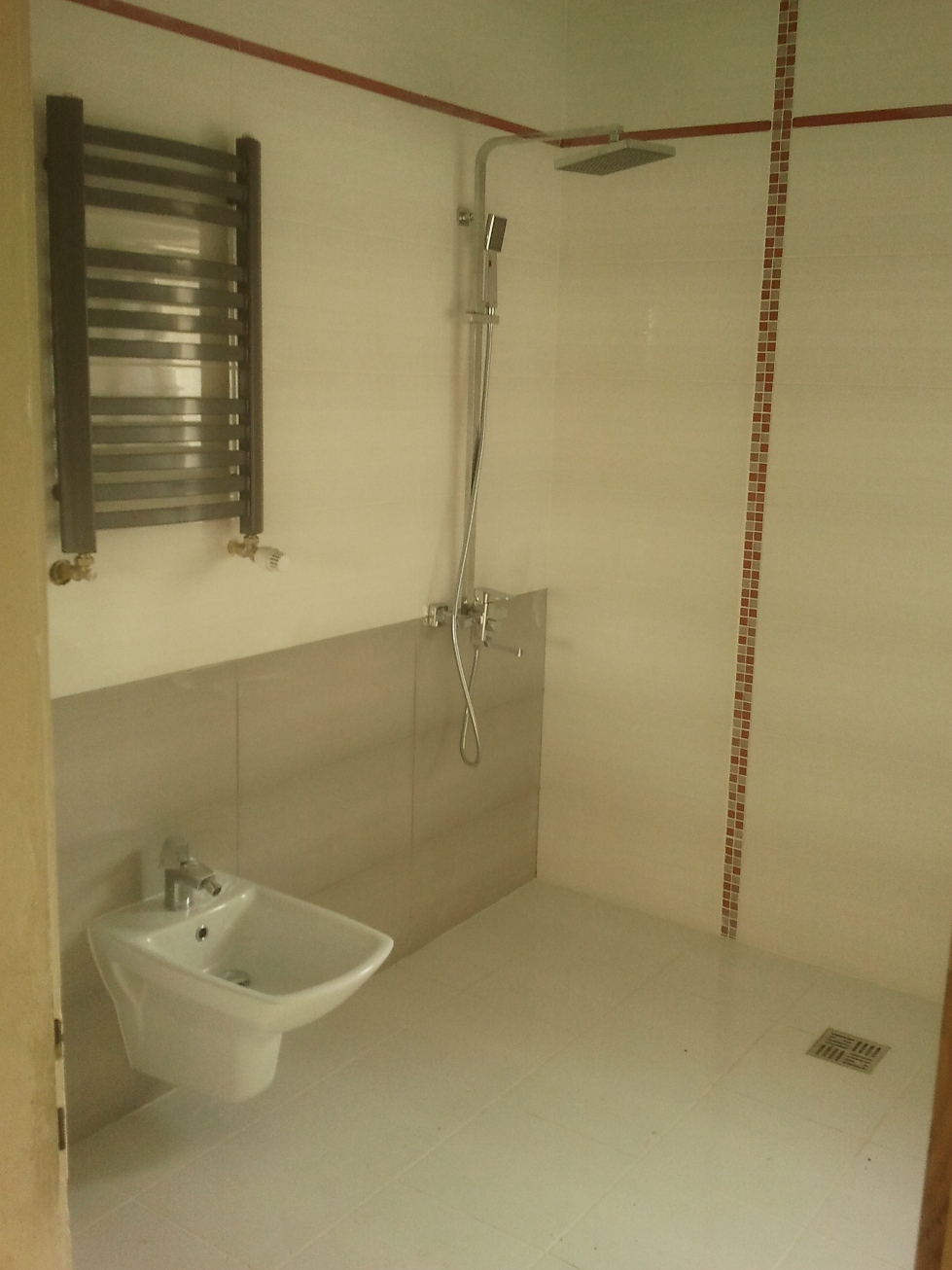 Wykończona łazienka z białymi płytkami, grzejnikiem drabinkowym, bidetem i kabiną prysznicową typu walk-in z odpływem liniowym w podłodze.