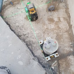 Instal-rem - Montaż podtynkowego zestawu prysznicowego z użyciem poziomicy laserowej DeWalt, widoczne przewody instalacji wodnej i fragment posadzki w trakcie prac instalacyjnych.