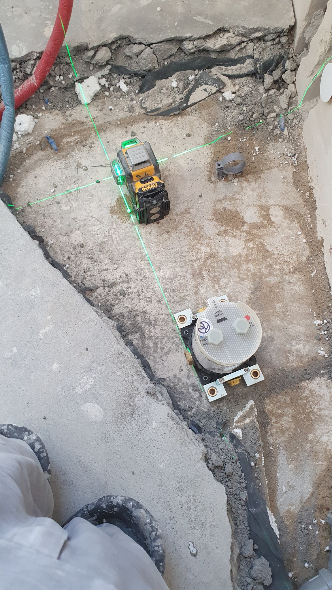 Montaż podtynkowego zestawu prysznicowego z użyciem poziomicy laserowej DeWalt, widoczne przewody instalacji wodnej i fragment posadzki w trakcie prac instalacyjnych.