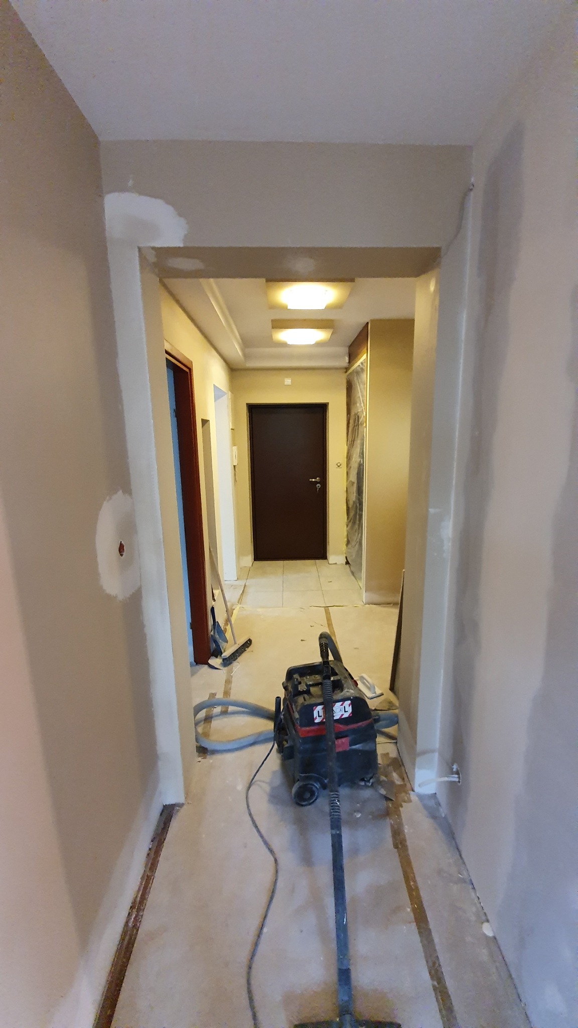 Korytarz w trakcie prac przygotowawczych do malowania: zagruntowane ściany, odkurzacz przemysłowy, widoczne ślady po listwach przypodłogowych.