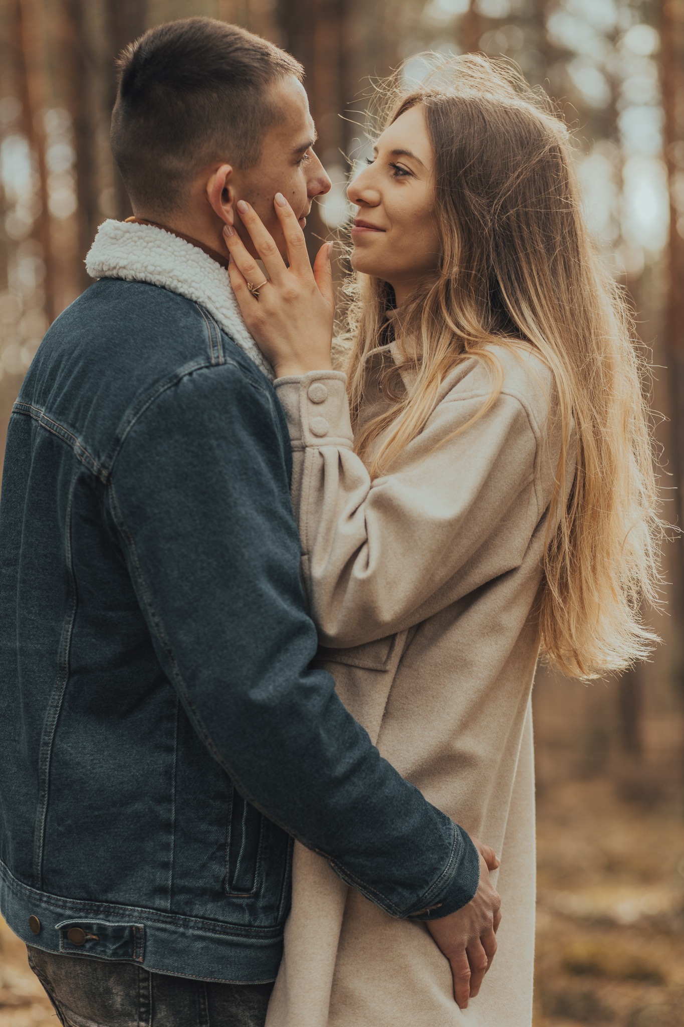 Młoda para w objęciach na tle jesiennego lasu, kobieta dotyka twarzy mężczyzny, na jej palcu widoczny złoty pierścionek w kształcie gwiazdy