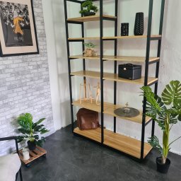 DM MET usługi spawalnicze - Regał metalowy z drewnianymi półkami, dekorowany roślinami doniczkowymi, figurką Baby Yoda i plakatem filmowym Kill Bill na tle ściany z cegły.