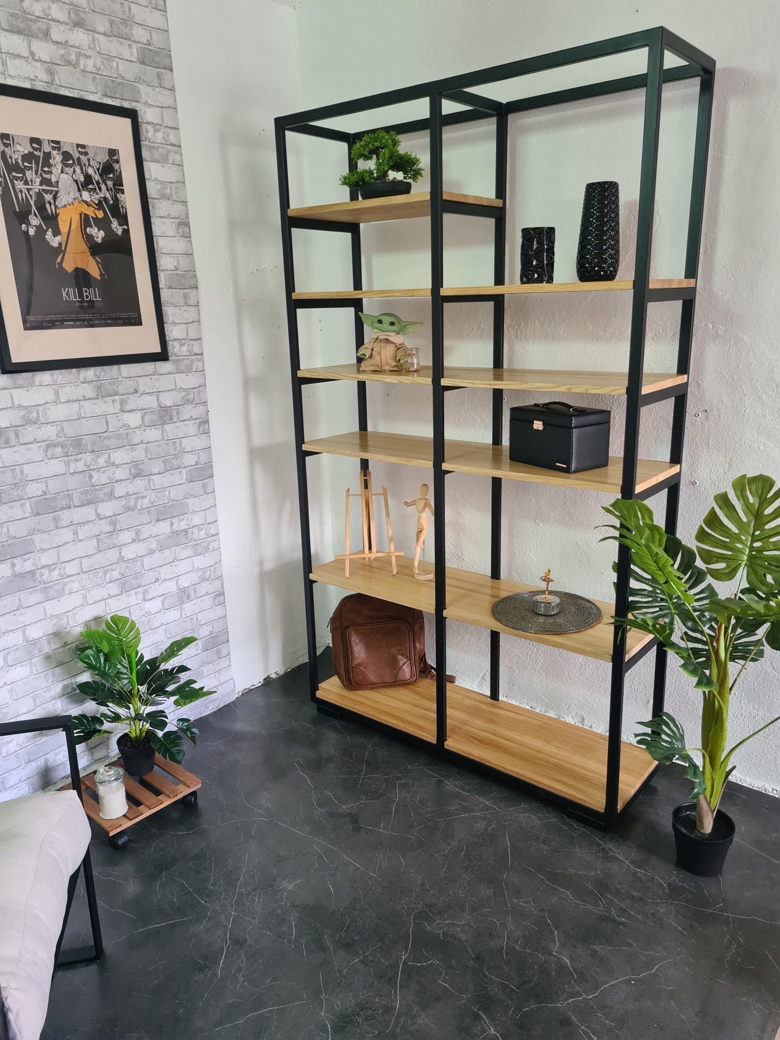 Regał metalowy z drewnianymi półkami, dekorowany roślinami doniczkowymi, figurką Baby Yoda i plakatem filmowym Kill Bill na tle ściany z cegły.