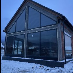 Pat-Mar Gliwice Sp. z o.o. - Dom w stanie surowym z dużymi, panoramicznymi oknami z czarnymi ramami. Widoczne ocieplenie pianką montażową. Zimowy krajobraz w tle.