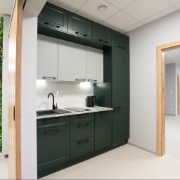 Boska Design - Nowoczesny aneks kuchenny w biurze: ciemnozielone szafki, jasnoszare fronty, białe płytki w jodełkę. Obok pionowy ogród, widok na salę konferencyjną i otwartą przestrzeń biurową.