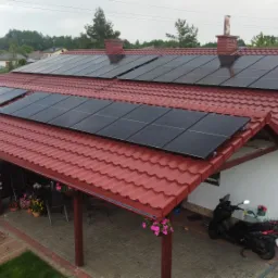 Dom jednorodzinny z czerwonym dachem pokrytym panelami fotowoltaicznymi, widok z góry, na podwórku skuter