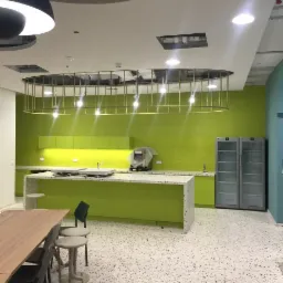 Wnętrze biura z limonkową kuchnią, blatem z lastryko, stołem jadalnym i dekoracyjnym oświetleniem sufitowym w kształcie elipsy z metalową konstrukcją.