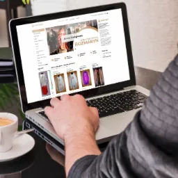 Osoba przegląda na laptopie sklep internetowy z szatami liturgicznymi, obok filiżanka espresso.