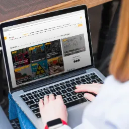 Osoba przegląda na laptopie stronę internetową z newsami z Krosna, siedząc na zewnątrz, widoczny zegarek na ręce.