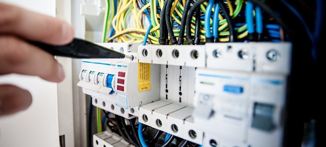Elektryk sprawdza napięcie w rozdzielnicy za pomocą próbnika napięcia, widoczne przewody w różnych kolorach.