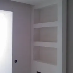 Wnęka z półkami w ścianie po remoncie, widoczny fragment grzejnika w dolnej części wnęki, ściany pomalowane na biało, surowy stan wykończenia.