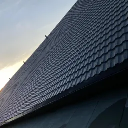 Nowy, ciemny dach z dachówki ceramicznej w promieniach zachodzącego słońca, widok z dołu pod kątem.