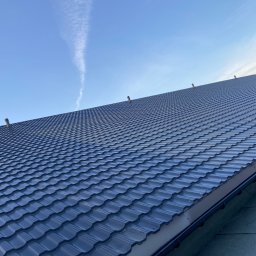 POLBLACH Imielnica - Nowy, ciemny dach z metalowej dachówki modułowej, widok z dołu, z kominkami wentylacyjnymi, na tle błękitnego nieba z smugą kondensacyjną