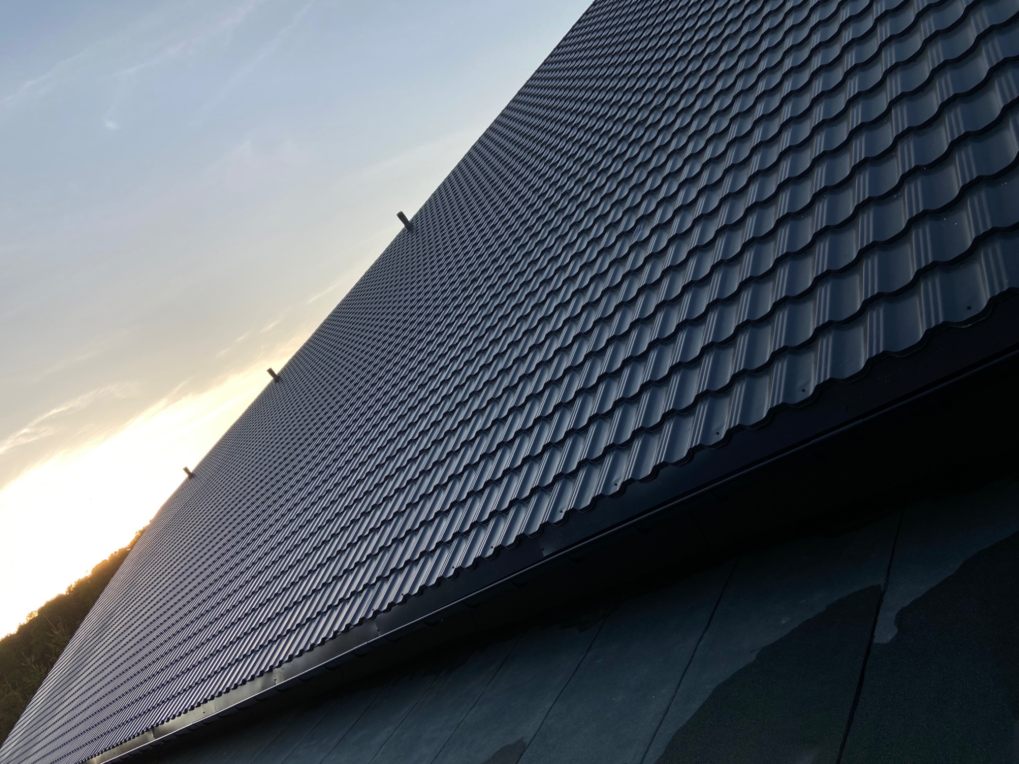 Nowy, ciemny dach z dachówki ceramicznej w promieniach zachodzącego słońca, widok z dołu pod kątem.