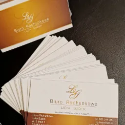 Stos wizytówek biura rachunkowego Lidia Gądek, z adresem, numerem telefonu i NIP, leżący na ciemnym blacie.