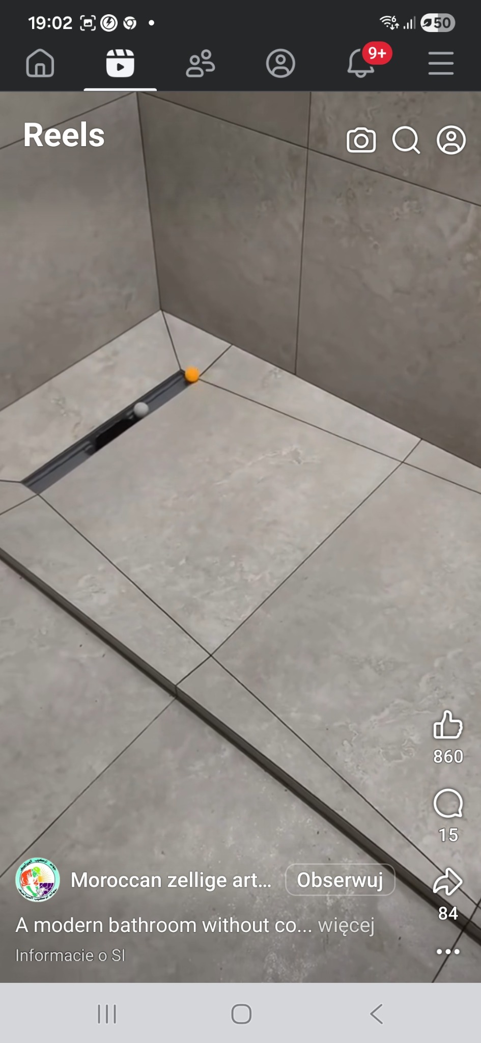 Beżowe płytki podłogowe w łazience z odpływem liniowym. Dwie kulki, pomarańczowa i biała, leżą na płytkach. Widok z góry, fragment podłogi i ściany.