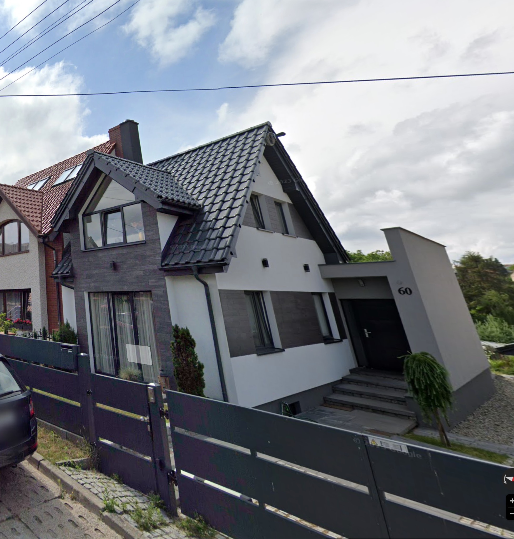 Dwukondygnacyjny dom jednorodzinny z nowoczesną elewacją w odcieniach bieli i szarości, z numerem 60 przy wejściu, widoczny zza szarego ogrodzenia.