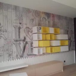 Pokój z fototapetą w stylu vintage z motywem anioła i napisu LOVE, uzupełniony białymi i żółtymi modułowymi półkami oraz niską szafką RTV.