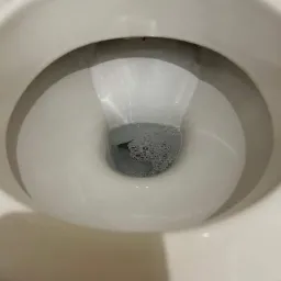 Wnętrze muszli klozetowej wypełnionej wodą z widocznymi pęcherzykami powietrza, ukazane z perspektywy z góry.