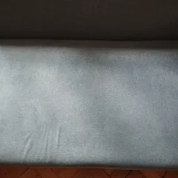 Szary narożnik z widoczną fakturą materiału i małą plamką na siedzisku, ujęcie z góry.