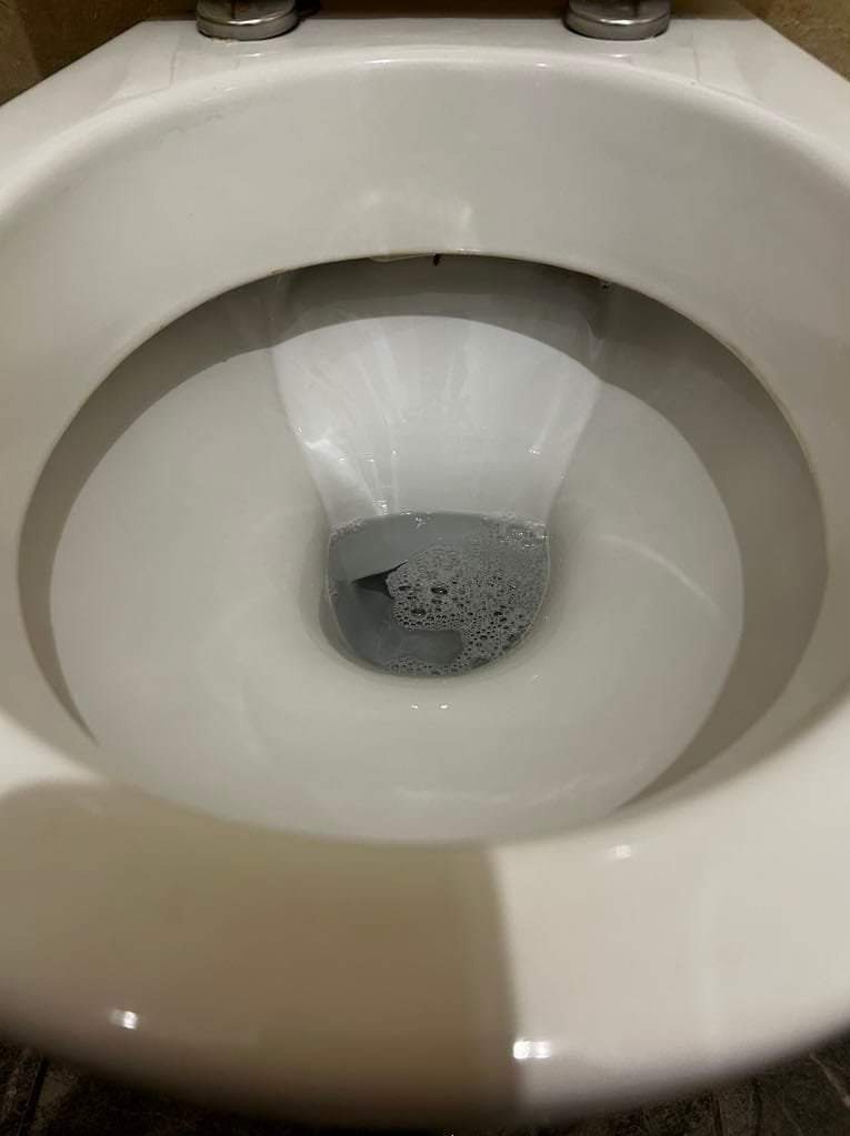 Wnętrze muszli klozetowej wypełnionej wodą z widocznymi pęcherzykami powietrza, ukazane z perspektywy z góry.