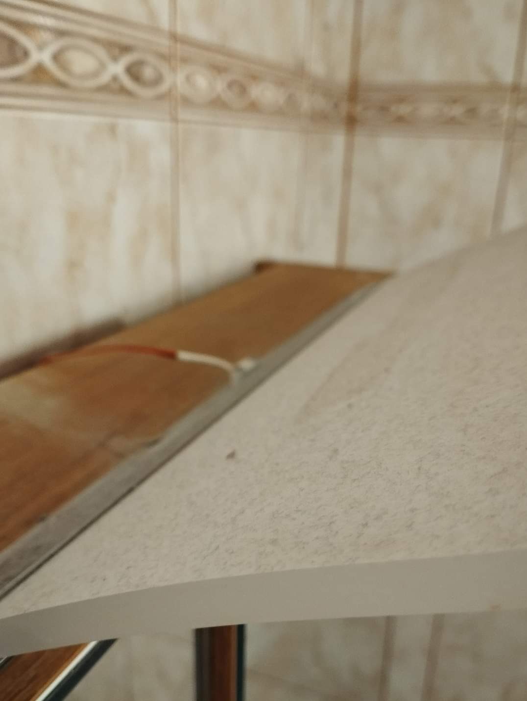 Zakurzona powierzchnia blatu w łazience z widocznymi płytkami ceramicznymi w tle.