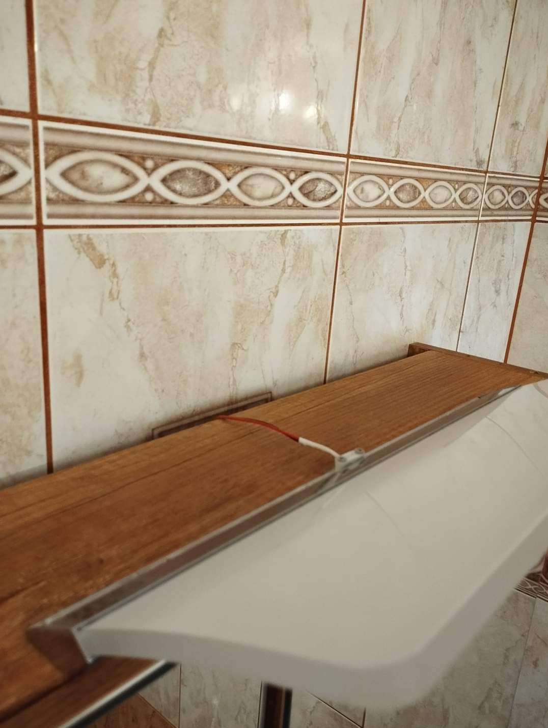 Umywalka zamontowana na drewnianej półce w łazience z beżowymi, wzorzystymi płytkami.