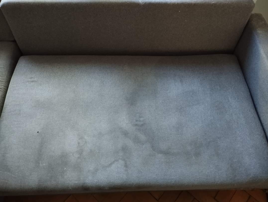 Szara kanapa z widocznymi plamami na siedzisku, ukazująca potrzebę odświeżenia tapicerki.