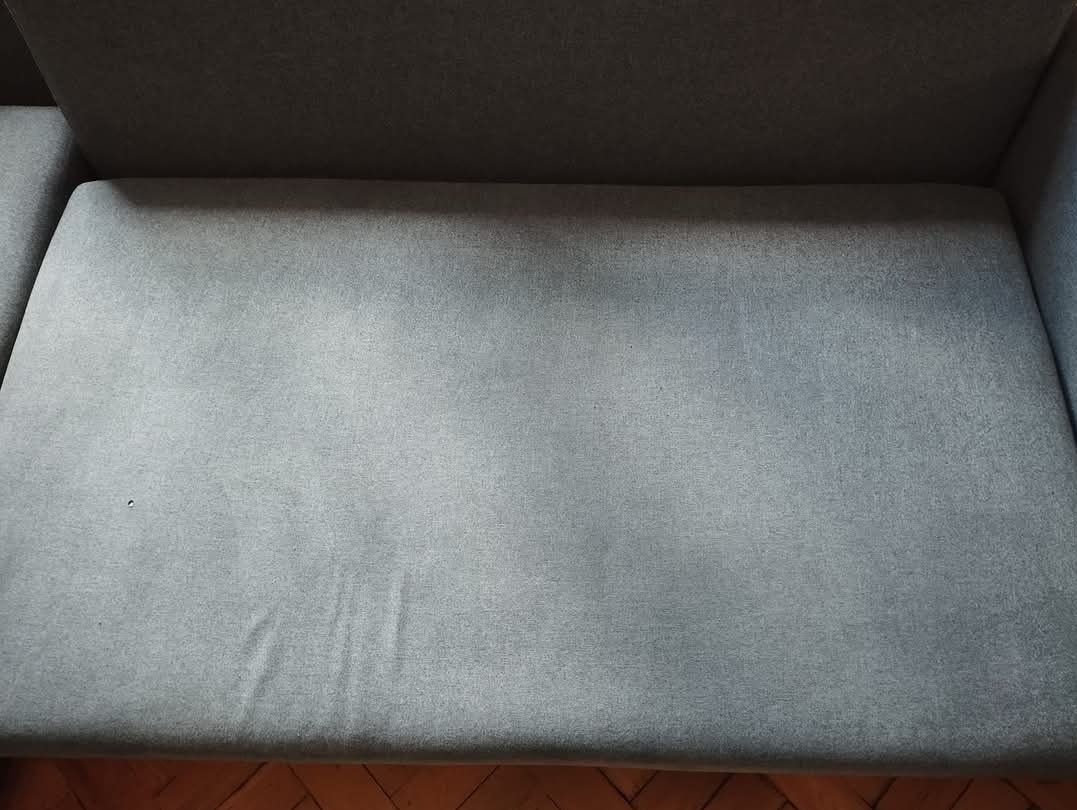 Szary narożnik z widoczną fakturą materiału i małą plamką na siedzisku, ujęcie z góry.