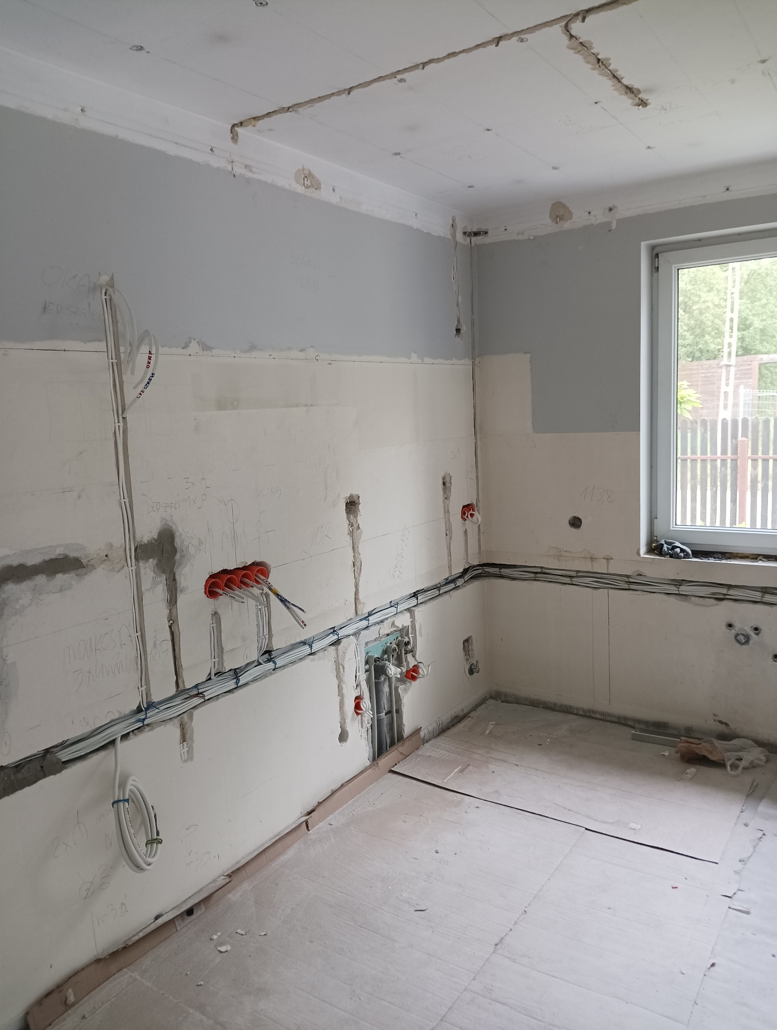 Wnętrze remontowanego domu jednorodzinnego z widoczną, częściowo zamontowaną instalacją elektryczną: kable prowadzone w ścianach, puszki instalacyjne i przewody na suficie, ściany w stanie surowym,...