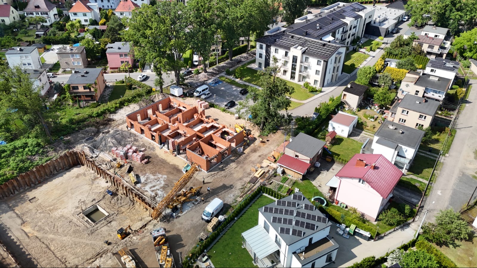 Budowa domu z czerwonej cegły w Jasieniu, widok z drona. Widoczne fundamenty, ściany w trakcie murowania, teren budowy i okoliczna zabudowa.