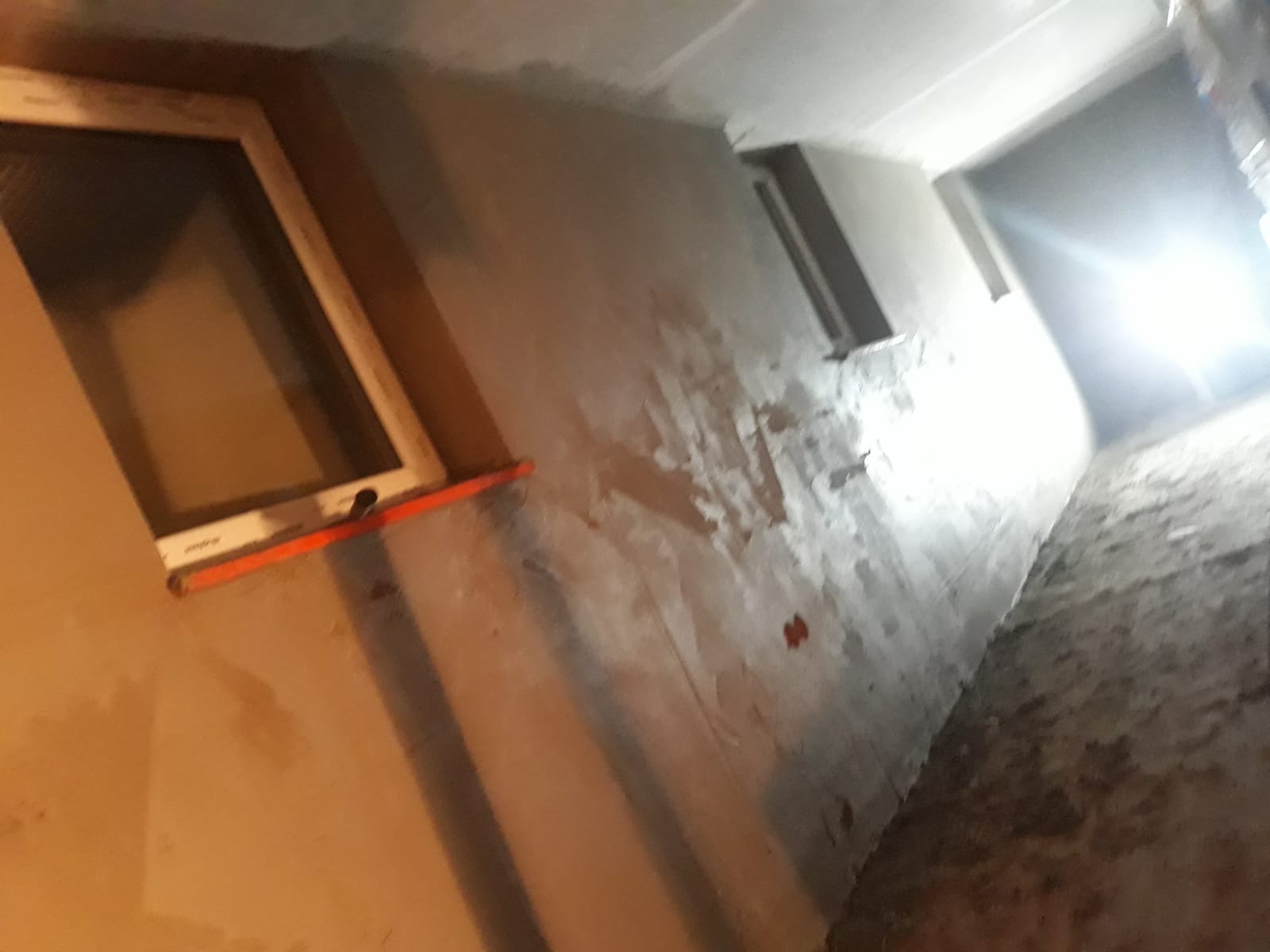 Świeżo nałożony tynk maszynowy na ścianie wewnętrznej z oknem, widoczne nierówności i ślady po narzędziach, przygotowanie do dalszych prac wykończeniowych.