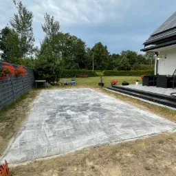 Ułożona szara kostka na przygotowanym podłożu, widok z góry na plac przydomowy, w tle dom z panelami słonecznymi i meble ogrodowe.
