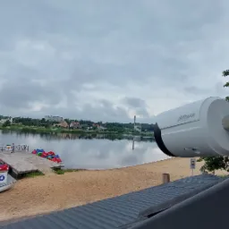 Kamera monitoringu Dahua zamontowana na dachu budynku z widokiem na jezioro, plażę i wypożyczalnię rowerków wodnych w tle.