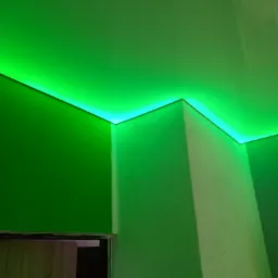 Nowoczesne oświetlenie LED w kolorze zielonym, zamontowane pod sufitem napinanym, oświetlające narożnik pokoju z widocznymi fragmentami drzwi.