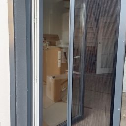 Volodymyr Vorobets - Rozsunięta moskitiera plisowana w grafitowej ramie, widok z zewnątrz na skrzydło okienne i wnętrze z kartonami. Ochrona przed owadami w nowoczesnym wydaniu.