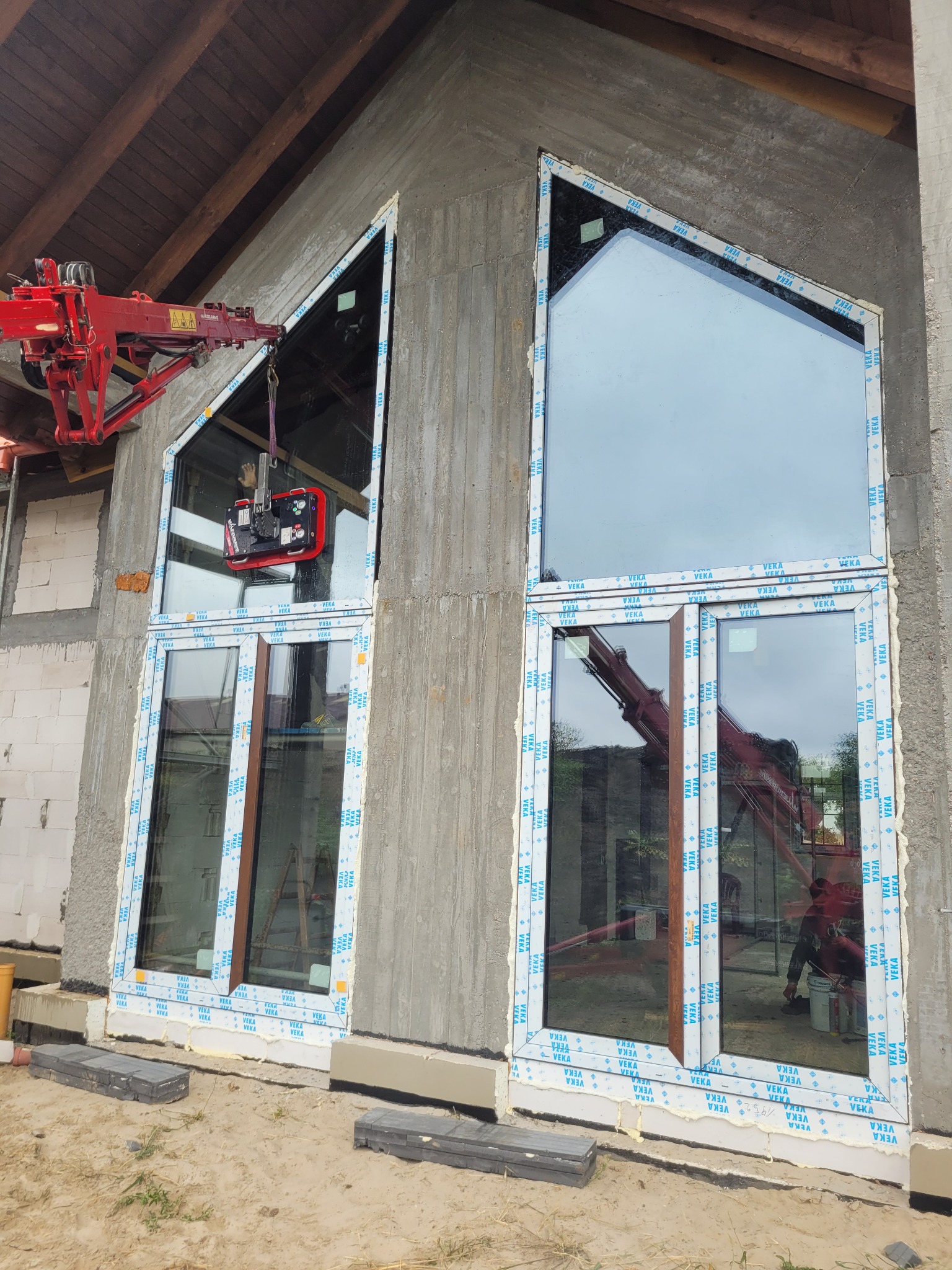 Montaż okien o nietypowym kształcie w surowym stanie budynku, widoczny dźwig z przyssawką do szkła, okna z profili oklejonych folią ochronną.