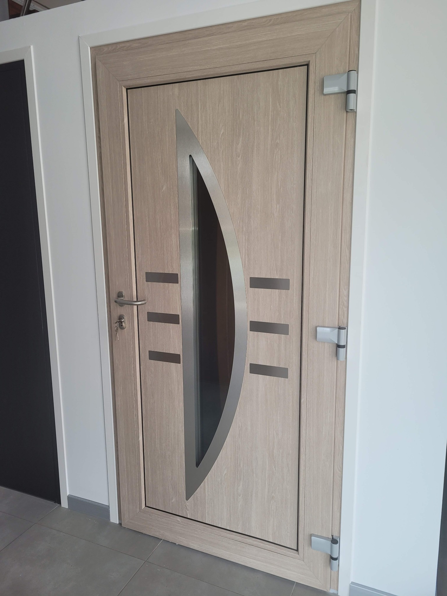 Zamknięte drzwi wewnętrzne z drewnopodobnym wykończeniem i owalnym przeszkleniem, zamontowane w Starogardzie Gdańskim, widoczne zawiasy i klamka z kluczem.