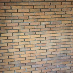 Grudziądz - Ściana z cegły klinkierowej w odcieniach pomarańczy i brązu, widoczne spoiny wypełnione szarą zaprawą, ułożona w regularny wzór.