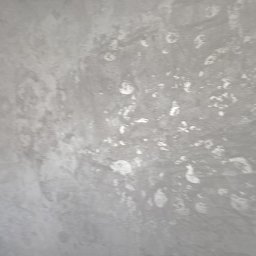 Grudziądz - Szara ściana z nieregularnymi, jaśniejszymi plamami, przypominającymi efekt dekoracyjny lub niedoskonałe wykończenie.