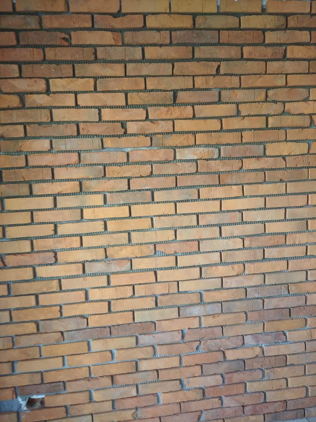 Ściana z cegły klinkierowej w odcieniach pomarańczy i brązu, widoczne spoiny wypełnione szarą zaprawą, ułożona w regularny wzór.