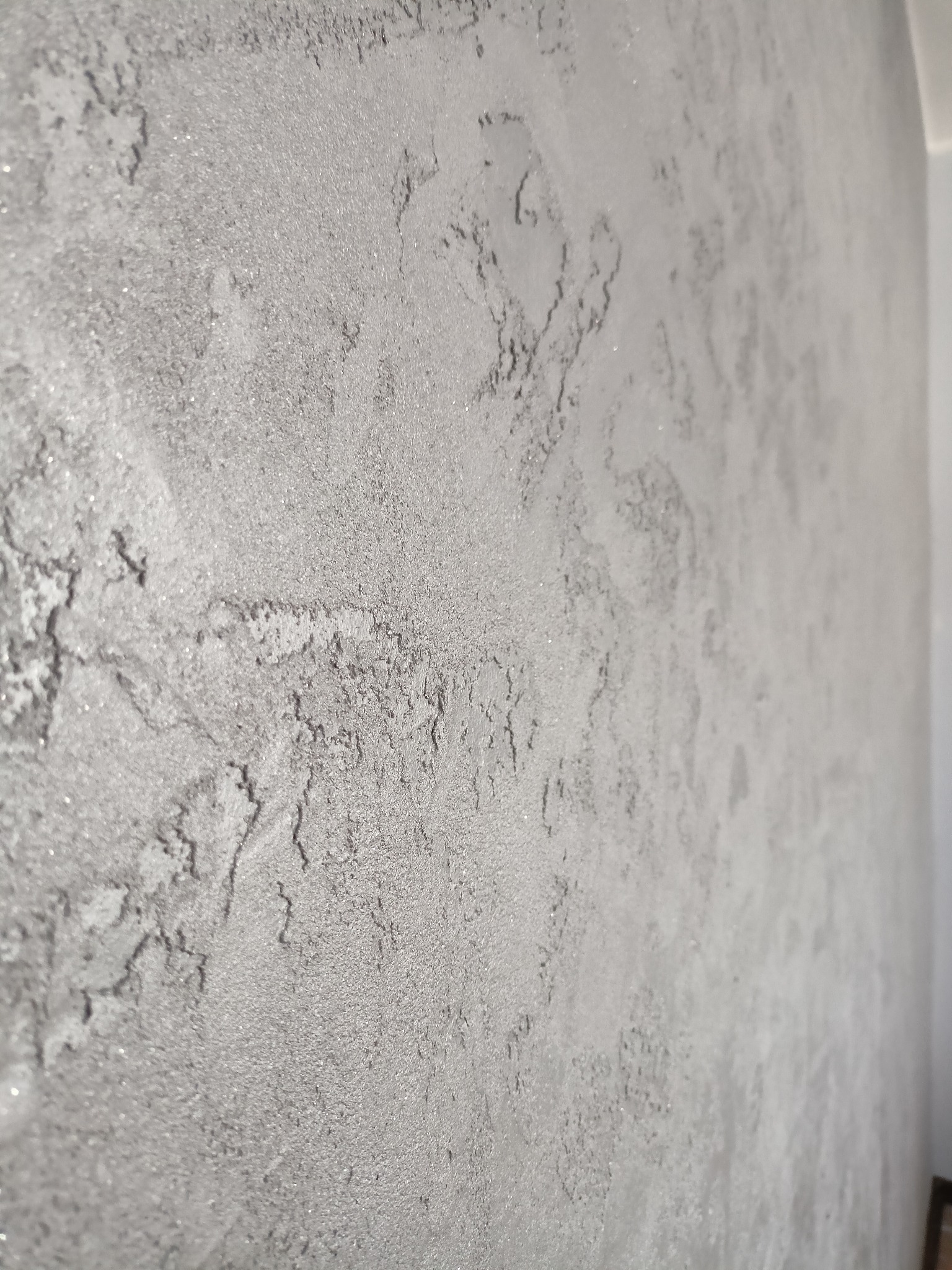 Szara ściana z dekoracyjną fakturą imitującą kamień, wykonana techniką szpachlowania z delikatnym połyskiem.