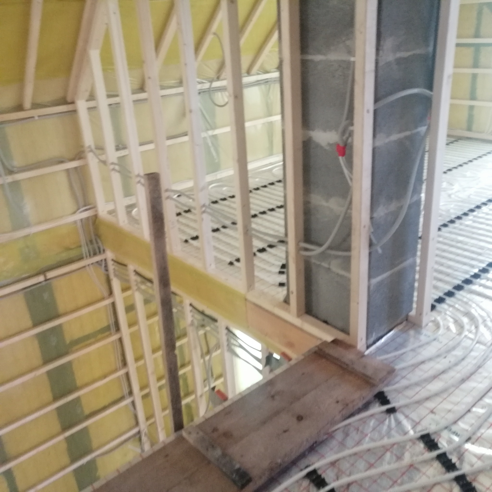 Wnętrze w trakcie remontu: widoczne ocieplenie poddasza wełną mineralną, drewniana konstrukcja szkieletowa ścian działowych oraz system ogrzewania podłogowego z rurami zamocowanymi do folii...